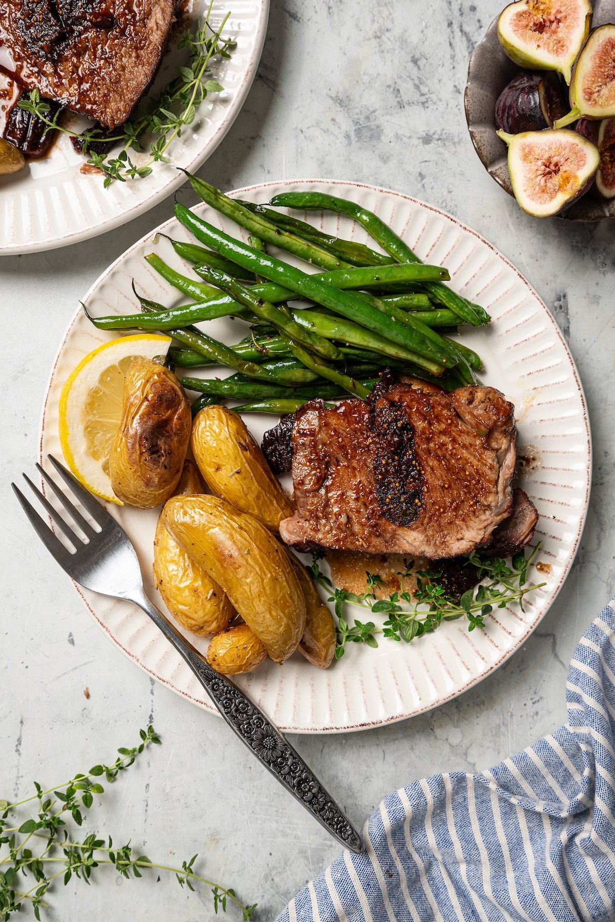 Serving plate of roasted pork shoulder recipe with green beans and mini potatoes on the side. 